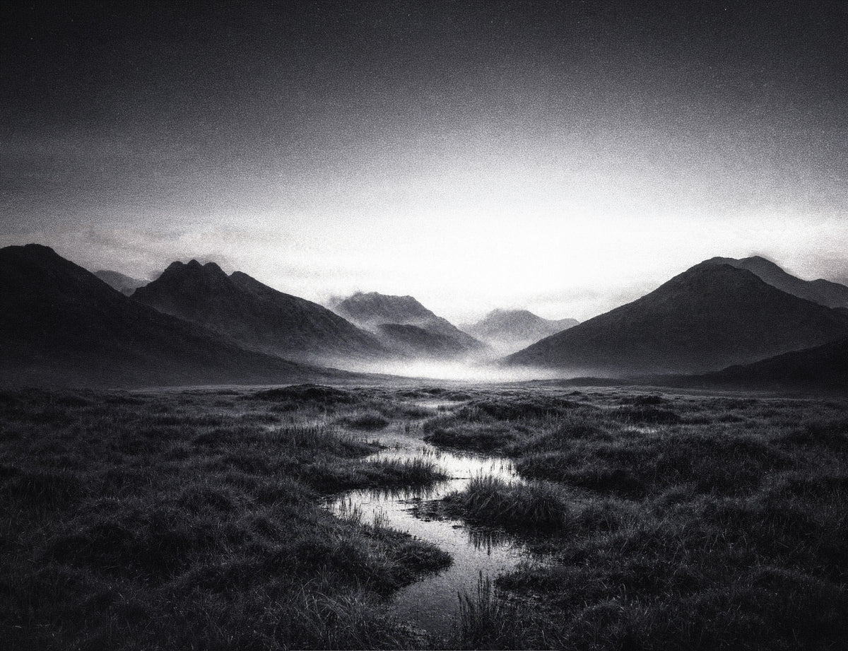 Black and white Nordic peat bog with a stream of water winding toward misty mountains