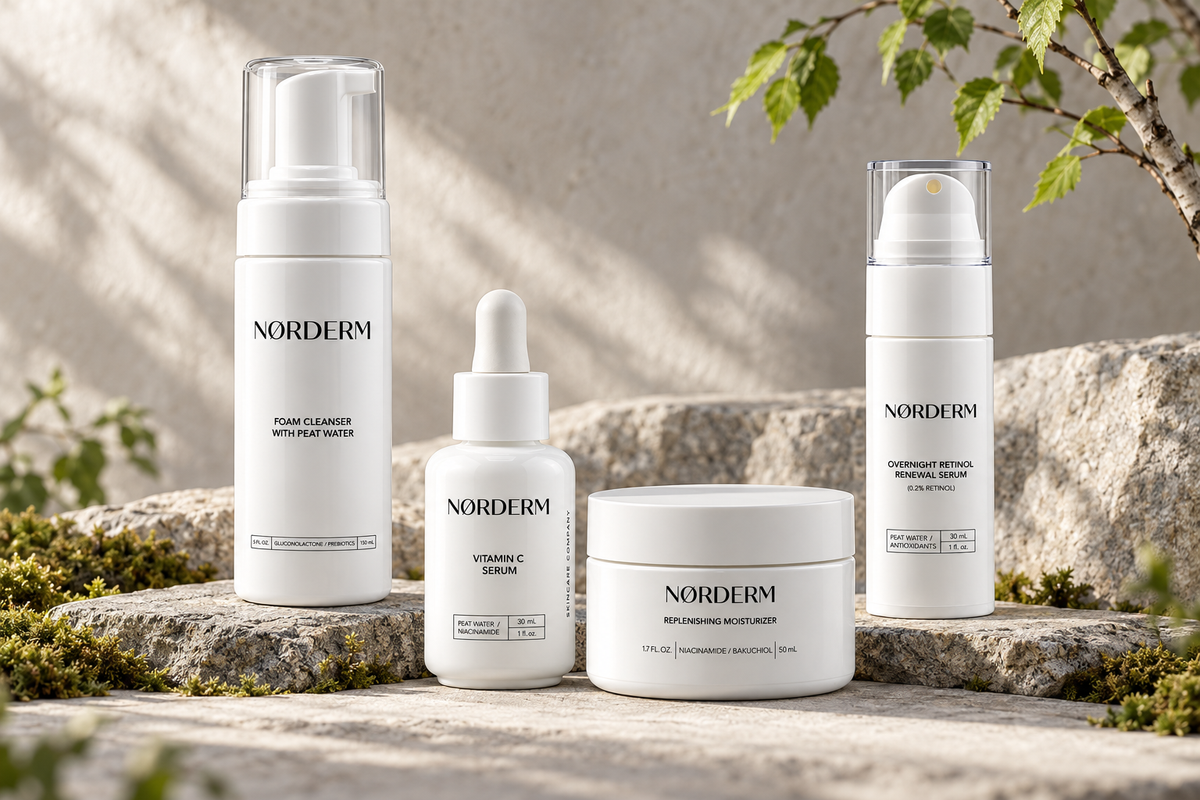 The four NØRDERM products on Nordic stone with moss and birch leaves in soft daylight